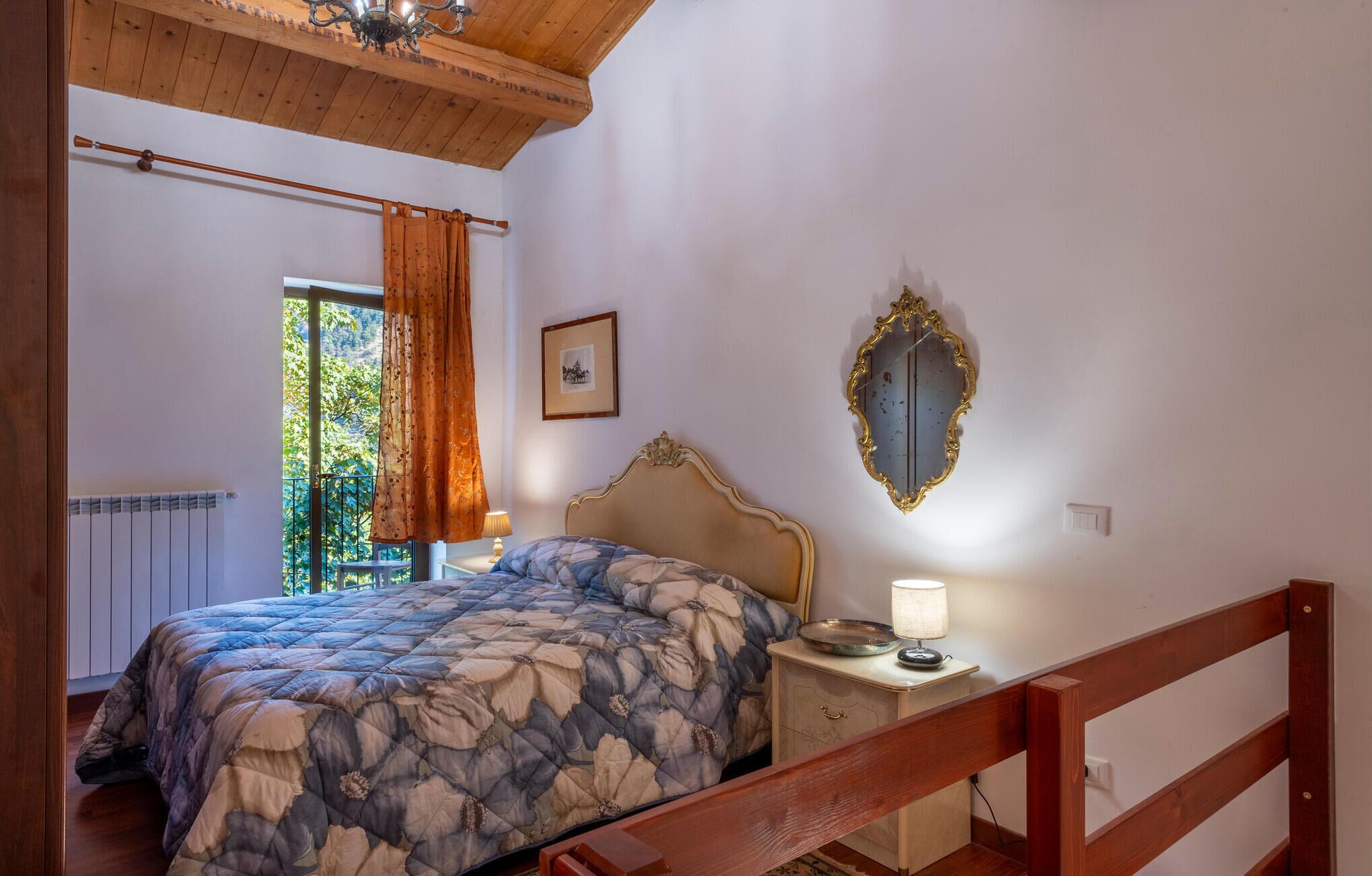 A bedroom with a bed, a nightstand, a mirror, and a window with curtains.