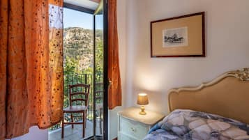Un dormitorio con cama, mesita de noche, lámpara, silla y un cuadro en la pared.