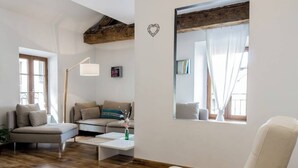 En moderne stue med sofa, hvid lænestol, sofabord og et stort spejl.