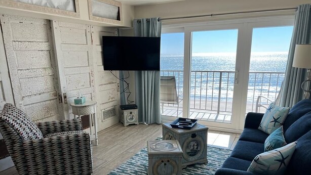 A living room with a sofa, a patterned armchair, a television, and a view of the ocean through large windows.