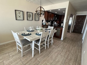Un coin repas avec une table dressée pour quatre personnes, entourée de chaises, et une cuisine en arrière-plan.
