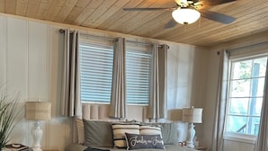 A bedroom with a bed, two bedside tables, a ceiling fan, and a window with curtains.