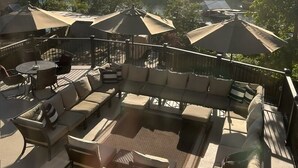 An outdoor deck with seating, umbrellas, and a view of a lake and trees.