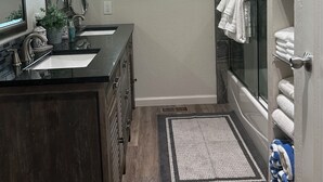 A modern bathroom with a double sink, a large mirror, a shower with glass doors, and a small window.