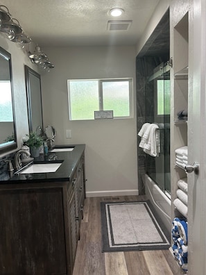Un bagno moderno con doppio lavandino, uno specchio grande, una doccia con pareti in vetro e un piccolo oblò.