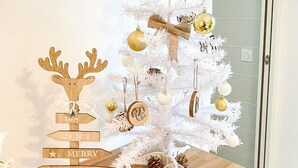 Ein weißer Weihnachtsbaum mit Dekorationen und einem Schild auf einem Holztisch.