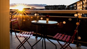 Ein Balkon mit Tisch und Stühlen, Blick auf den Sonnenuntergang und Gebäude im Hintergrund.
