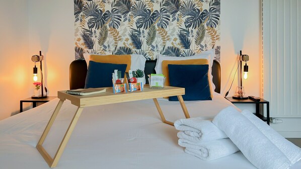 A neatly made bed with a wooden bedside table, a nightstand, and a tropical-themed tapestry. - Woody 100m du lac balcon (Annecy)
