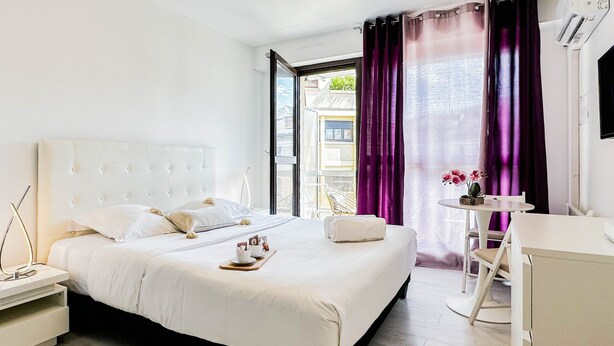 Ein modernes Hotelzimmer mit einem großen Bett, einem Nachttisch, einem kleinen Schreibtisch und einem Sessel.