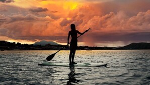 Eine Person steht auf einem Paddleboard auf dem Wasser, im Hintergrund ein Sonnenuntergang.