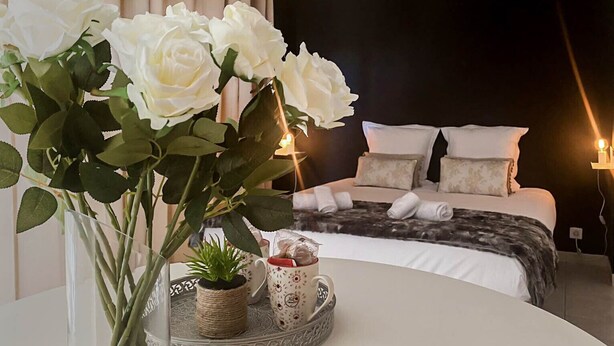 Un dormitorio con una cama, almohadas y una mesita de noche con un jarrón de flores blancas.