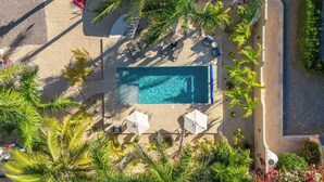 Eine Vogelperspektive eines Resorts mit Schwimmbad, Liegestühlen und Palmen.