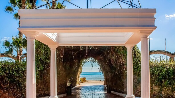 Una pérgola blanca con columnas que da a vista al mar.