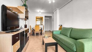 Una sala de estar moderna con una televisión de pantalla plana, muebles de madera, un sofá verde y un comedor con un espejo.