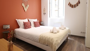 A bedroom with a large bed, a bedside table with a lamp, a window, and a wall hanging. - Secrets d ambre rue royale (Annecy)