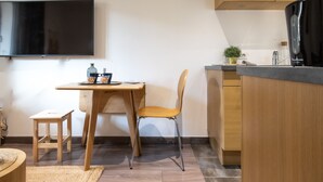 A compact kitchen with a wooden table, a chair, a small stool, and a TV mounted on the wall. - Secrets d ambre rue royale (Annecy)