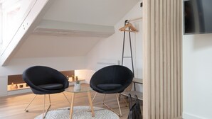 Een moderne loft slaapkamer met schuine plafonds, een glazen tafel met twee zwarte stoelen, een televisie aan de muur en een houten vloer.