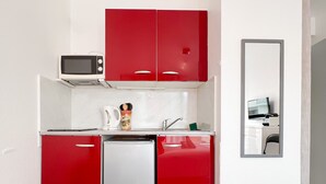 Une cuisine compacte avec des meubles rouges, un four à micro-ondes, une machine à café et un petit réfrigérateur.