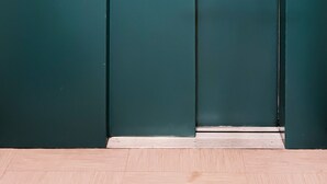 Une porte d’ascenseur de couleur turquoise, fermée, avec un panneau de commande situé sur le côté droit.
