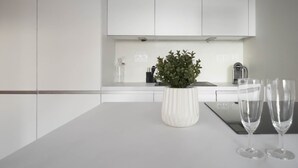 A modern kitchen with white cabinetry, a central island with a white vase and two wine glasses, and a small potted plant. - Django 400 m du lac (Annecy)