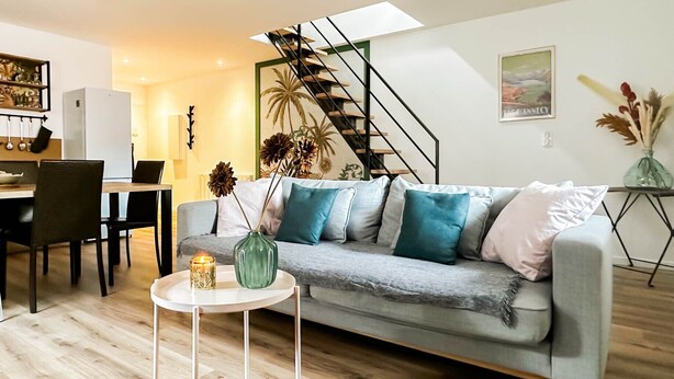 A modern living room with a grey sofa, a small white side table, a green vase, and a staircase. - Rainbow rue carnot 4 adultes et 1 enfant (Annecy)