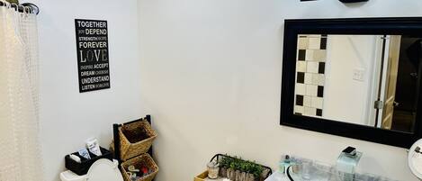 Et badeværelse med toilet, en vask med en glas skål, et spejl og et motiverende citat på væggen.