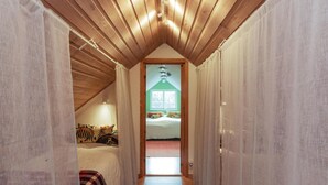 Un pasillo estrecho con vigas de madera en el techo, una cama con ropa de cama colorida y una ventana con vistas a árboles.