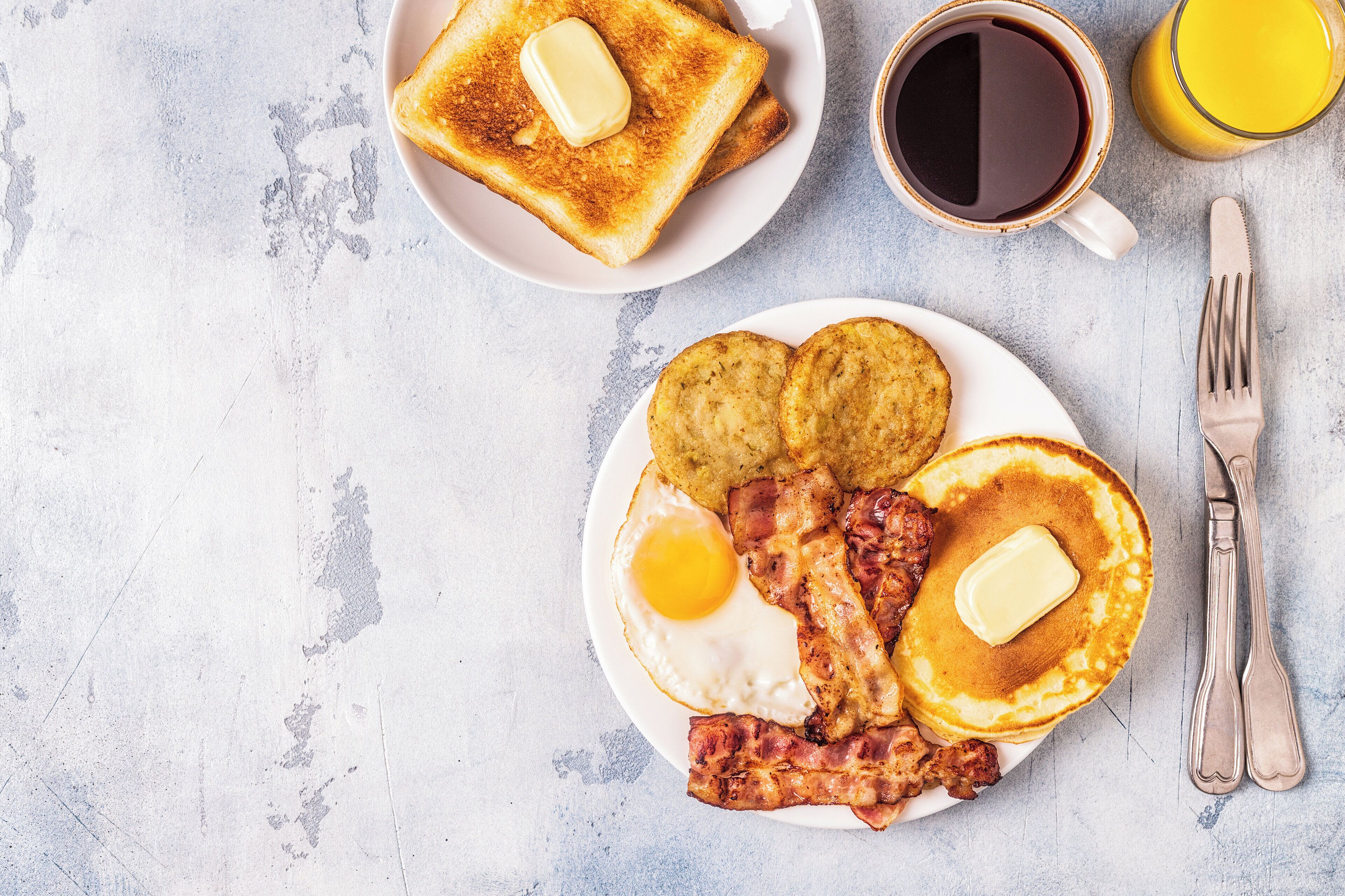 A breakfast plate with toast, eggs, bacon, and pancakes, accompanied by a cup of coffee and a glass of orange juice.