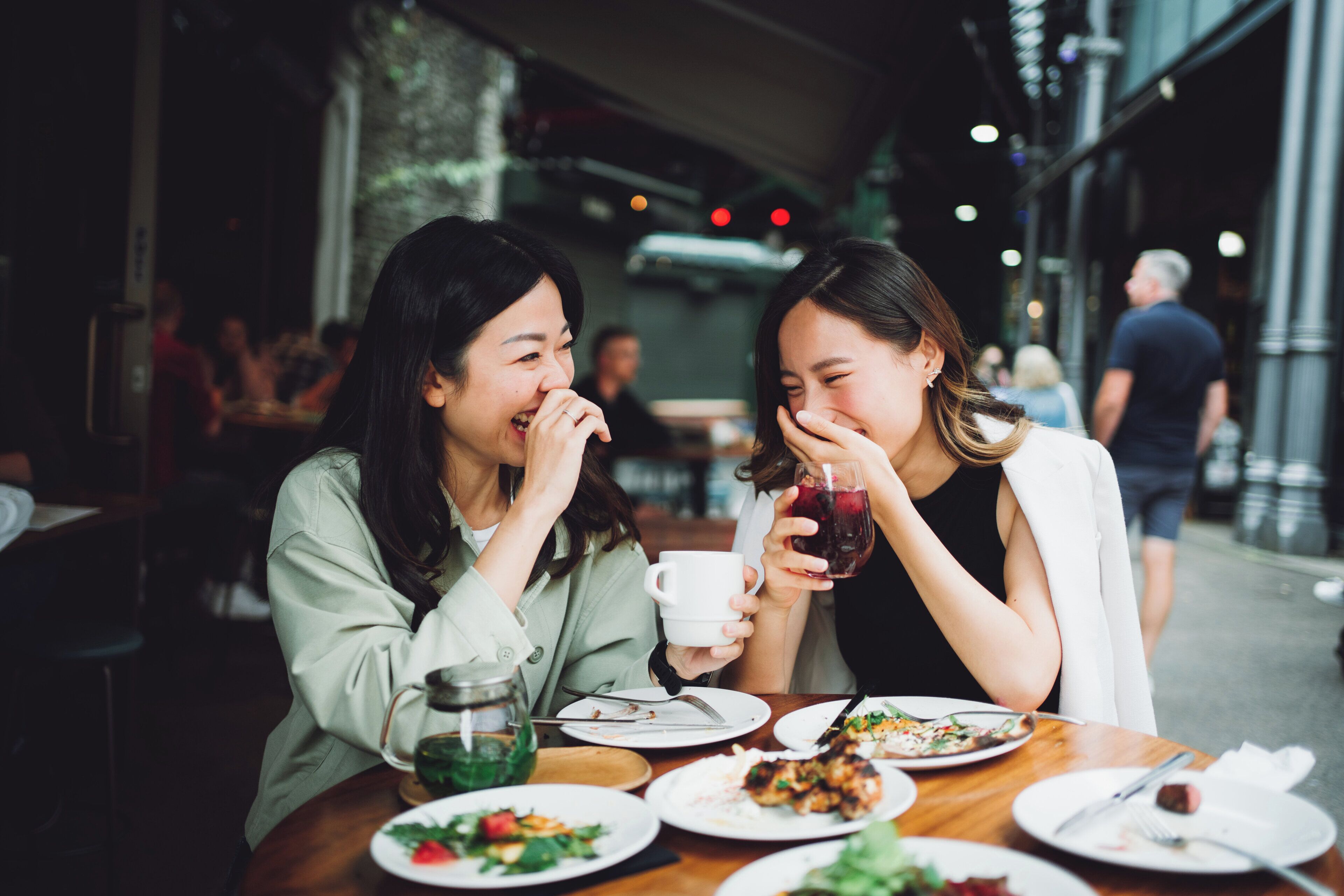 Two people dining at an outdoor table with various dishes and drinks.