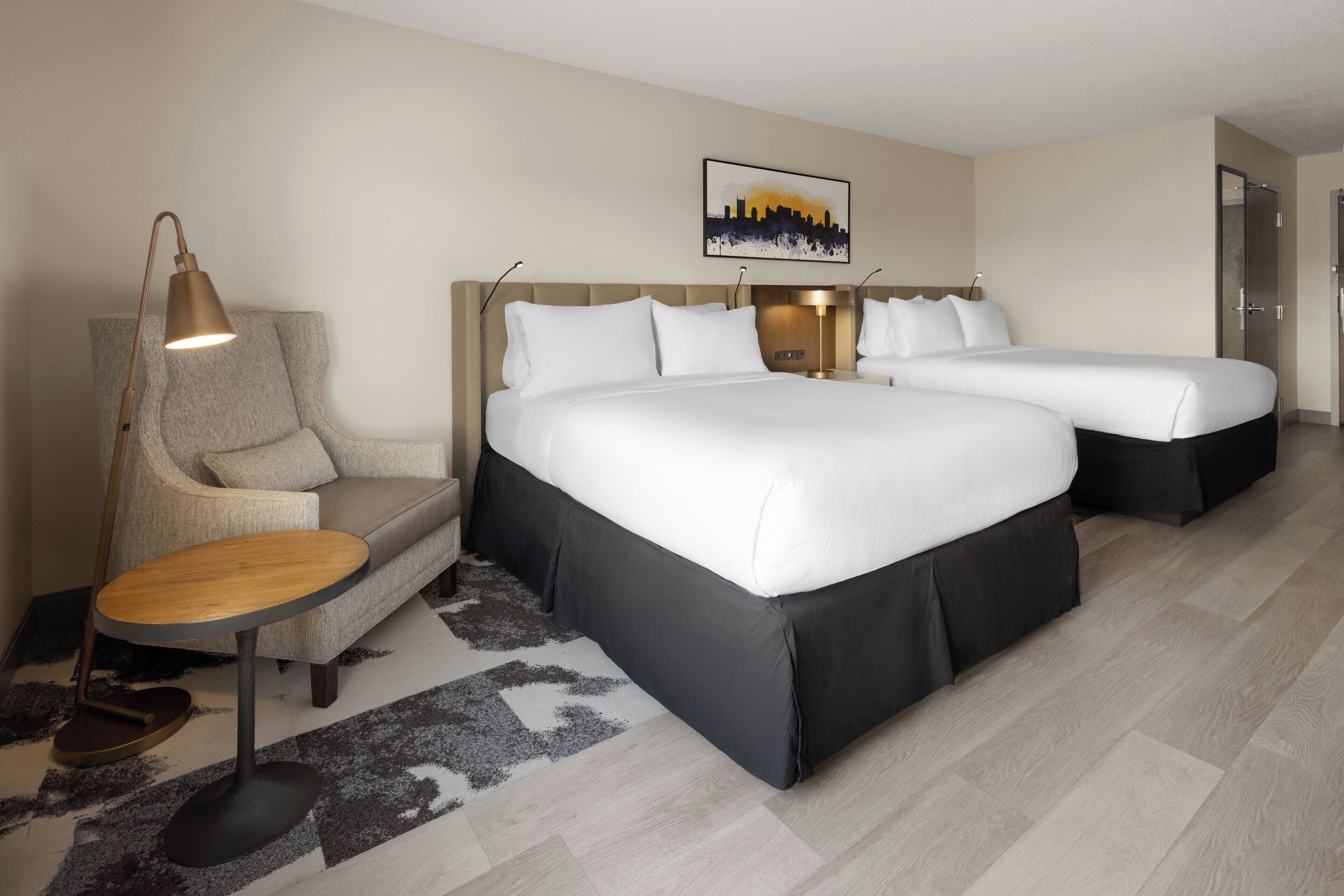 A hotel room with two beds, a sofa, a desk, and a cityscape artwork on the wall.