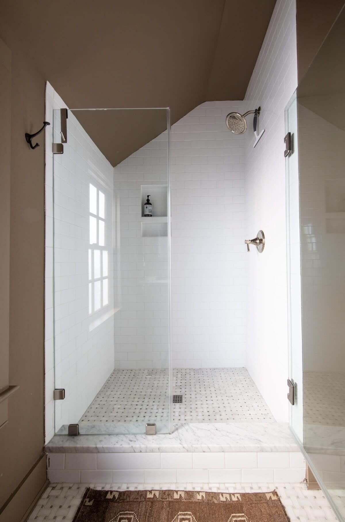 A walk-in shower with a glass door, white tiled walls, and a marble floor.