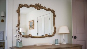Une coiffeuse agrémentée d’un grand miroir décoratif, d’une lampe et d’un vase contenant des plantes de coton.