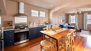 Une cuisine spacieuse avec des meubles de couleur bleu foncé, une cuisinière en acier inoxydable et une grande table à manger entourée de chaises en osier.