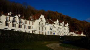 Eine Reihe weißer, mehrstöckiger Gebäude mit Balkonen, vor einer Kulisse aus Bäumen und blauem Himmel.