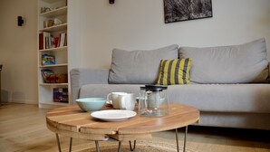 Ein Wohnzimmer mit grauem Sofa, einem Holztisch, einem Bücherregal und einem gerahmten Bild an der Wand.