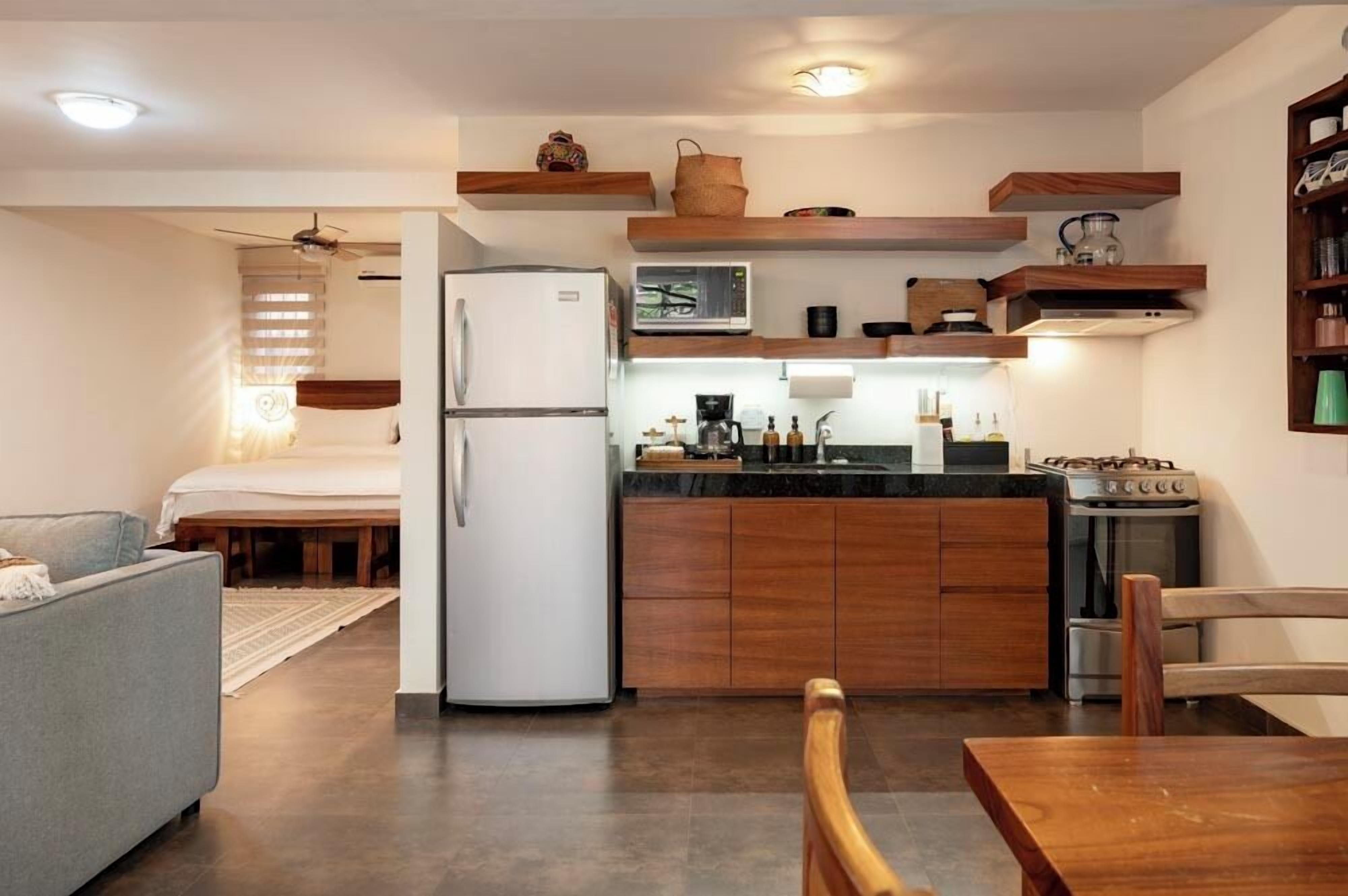 A compact kitchen with wooden cabinets, a refrigerator, a microwave, and a stove.