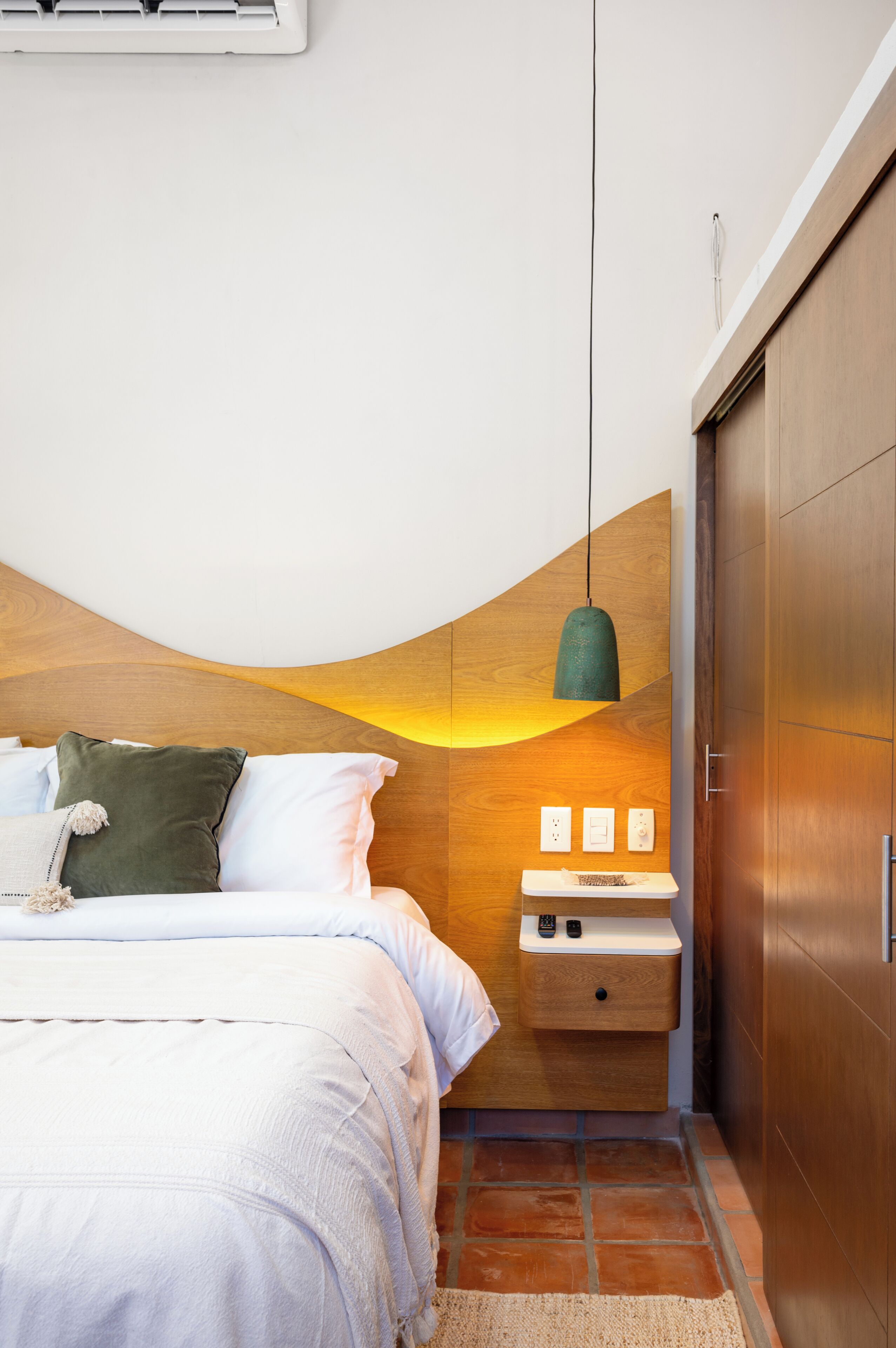 Een slaapkamer met een houten hoofdbord, een nachtkastje met een lamp en een bed met witte lakens.