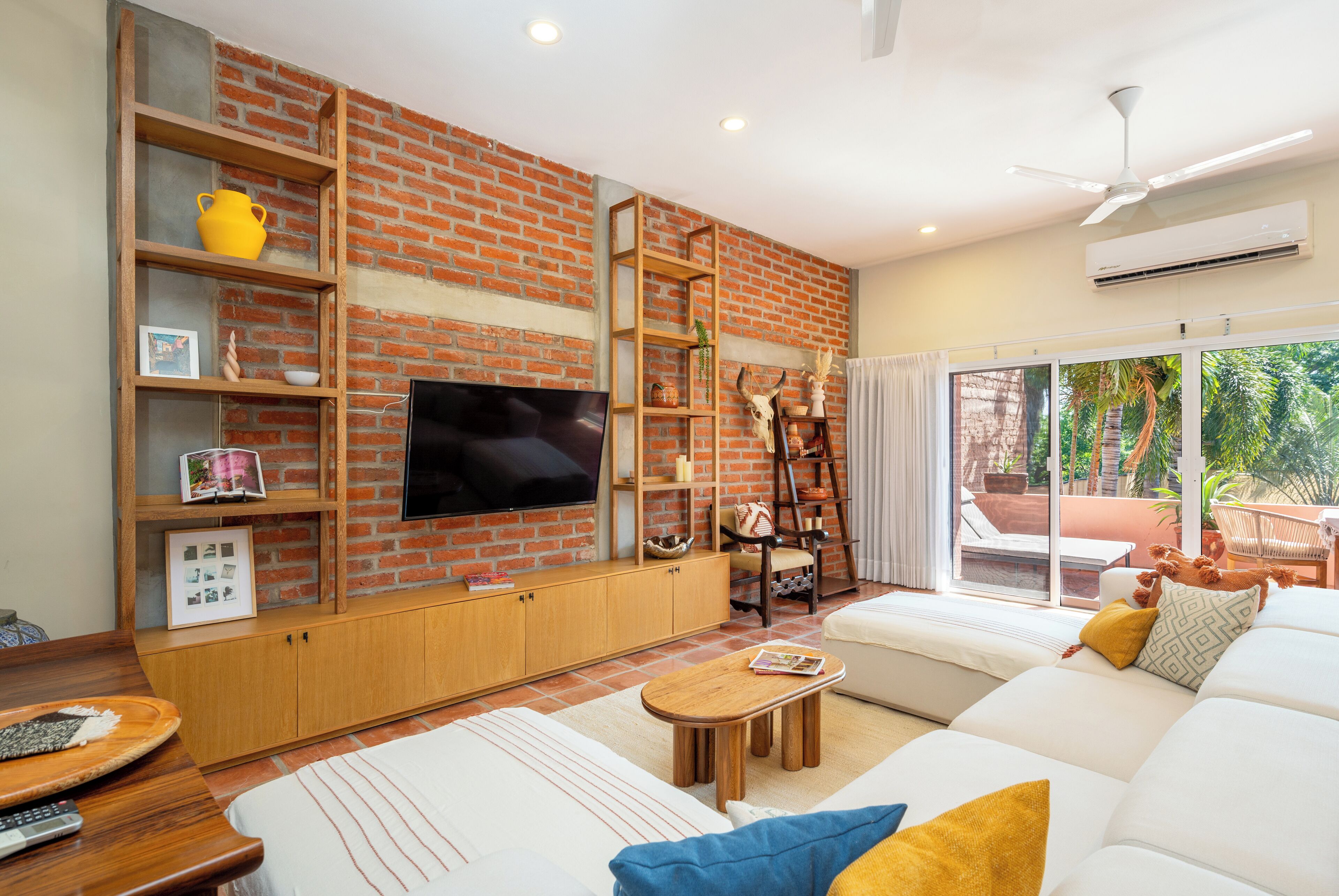 A modern living room with a brick wall, a flat-screen TV, a sofa, a coffee table, and a bookshelf.