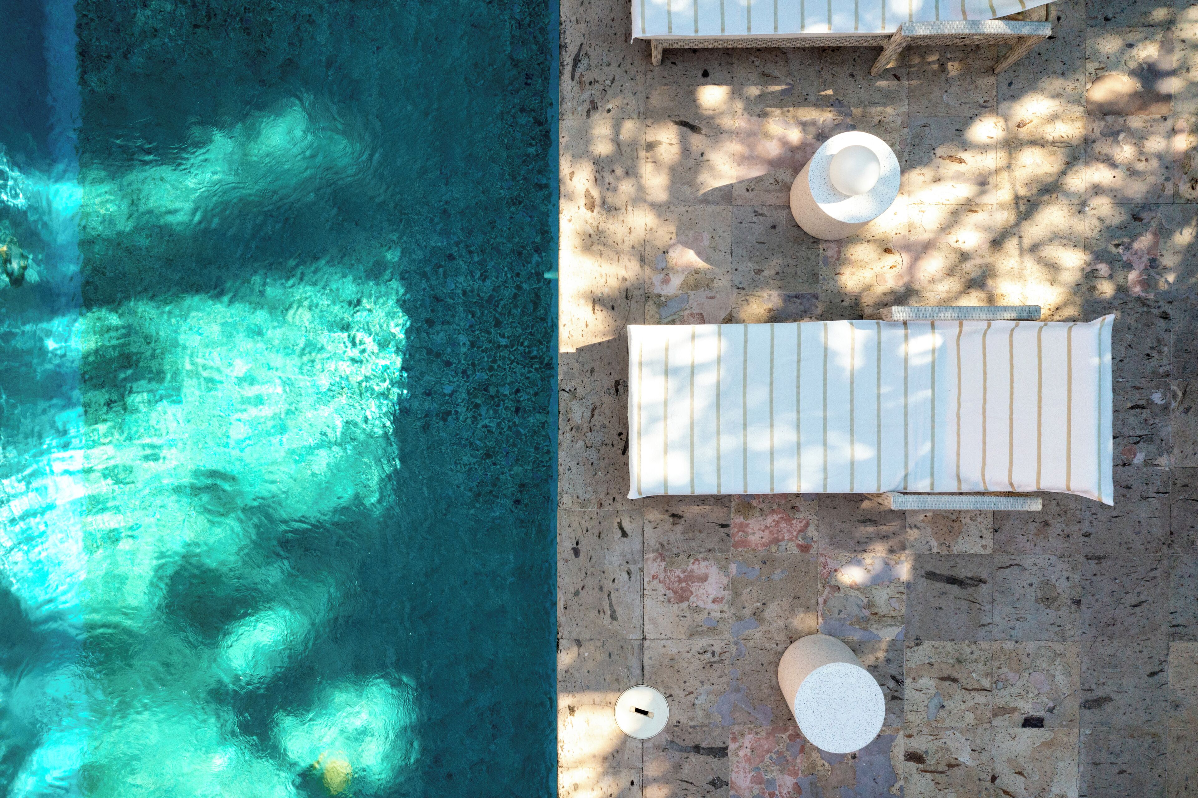 Vue aérienne d’un espace piscine avec des chaises longues et des transats sur une terrasse en pierre.