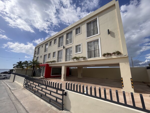 A multi-story building with balconies, a parking area, and a clear sky. - Palmares Suites (La Romana)