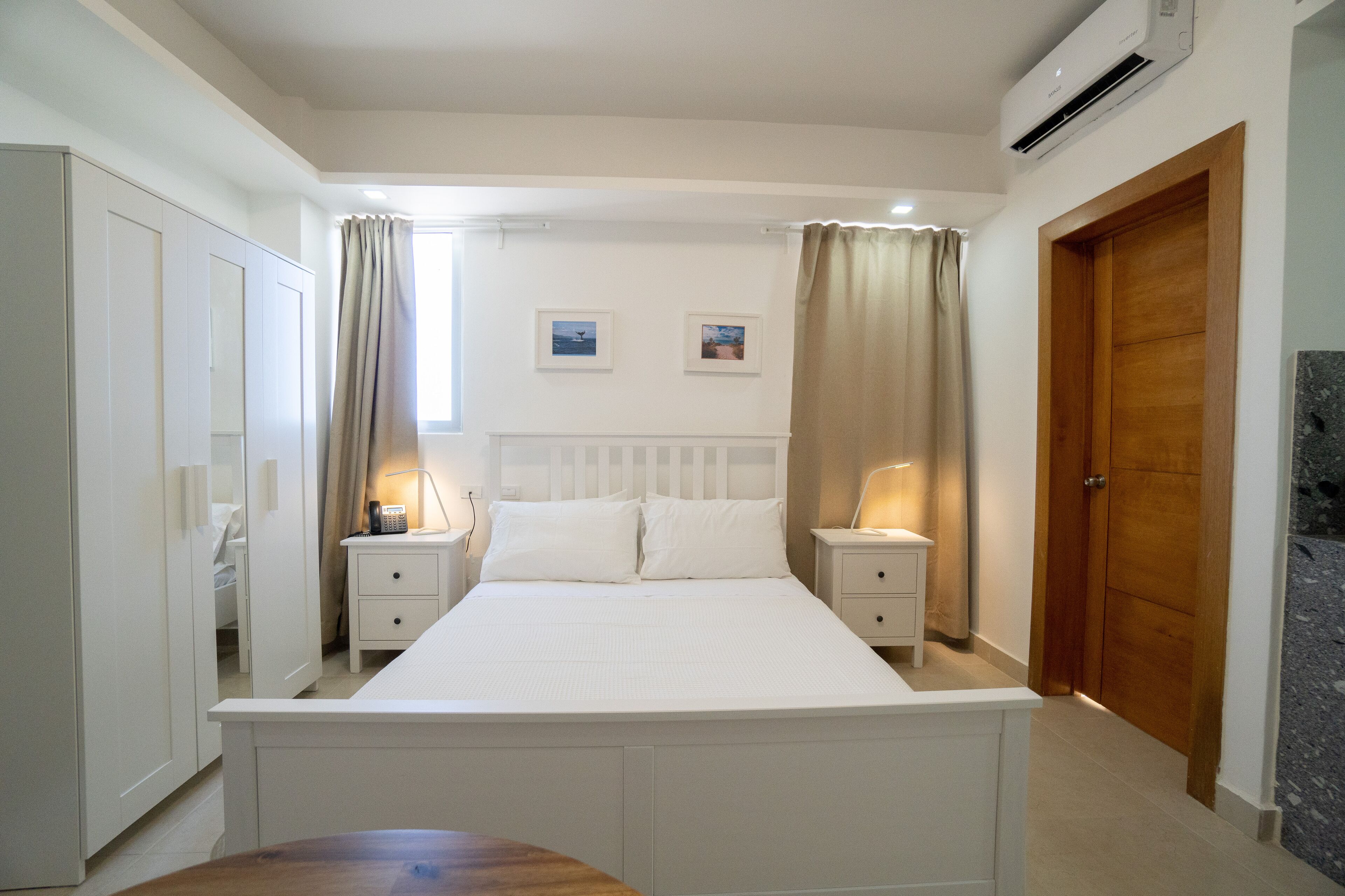 A bedroom with a large bed, two bedside tables with lamps, a wardrobe, and a door.