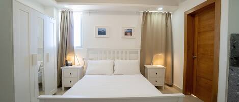 A bedroom with a large bed, two bedside tables with lamps, a wardrobe, and a door.