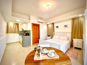 Une chambre d’hôtel comprenant un lit, une table de chevet, un petit bureau, une kitchenette et un coin repas avec une table mise pour le petit-déjeuner.