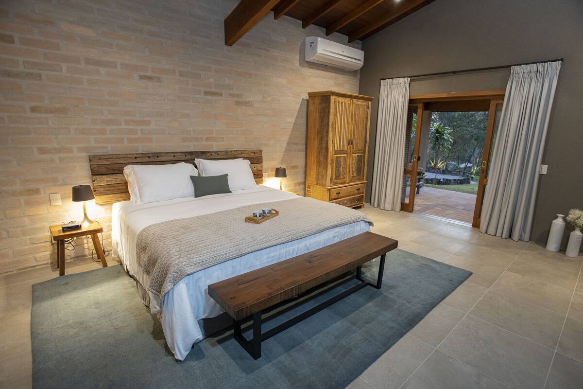 Un dormitorio con una cama grande, cabecera de madera, un banco, una mesita de noche y un armario.