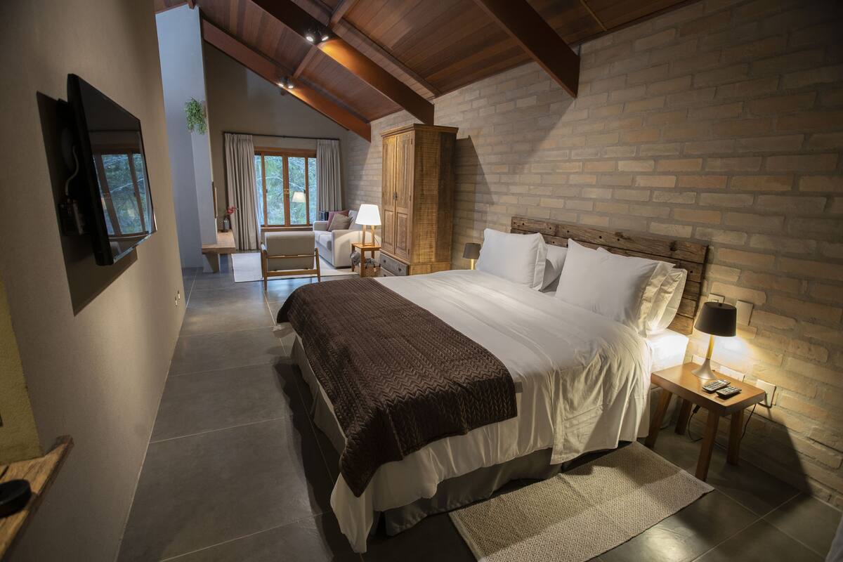 Un dormitorio con una cama grande, un armario de madera, una mesita de noche con lámpara y un televisor fijado en la pared.