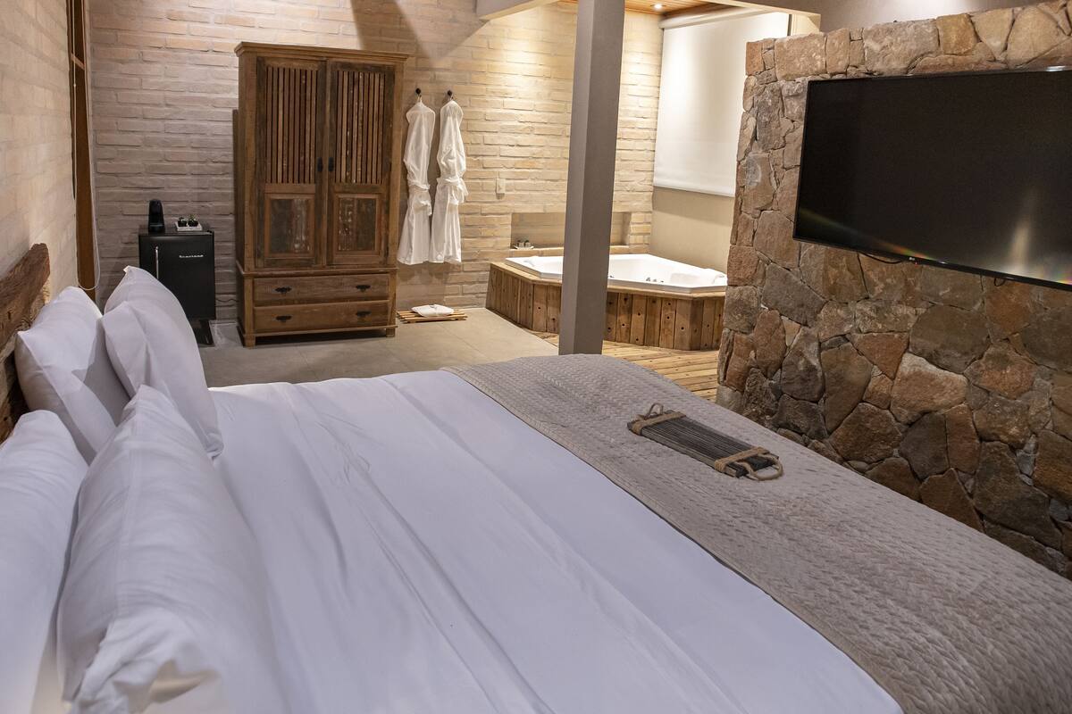 Un dormitorio con cama, armario de madera, pared de piedra y televisor montado en la pared.