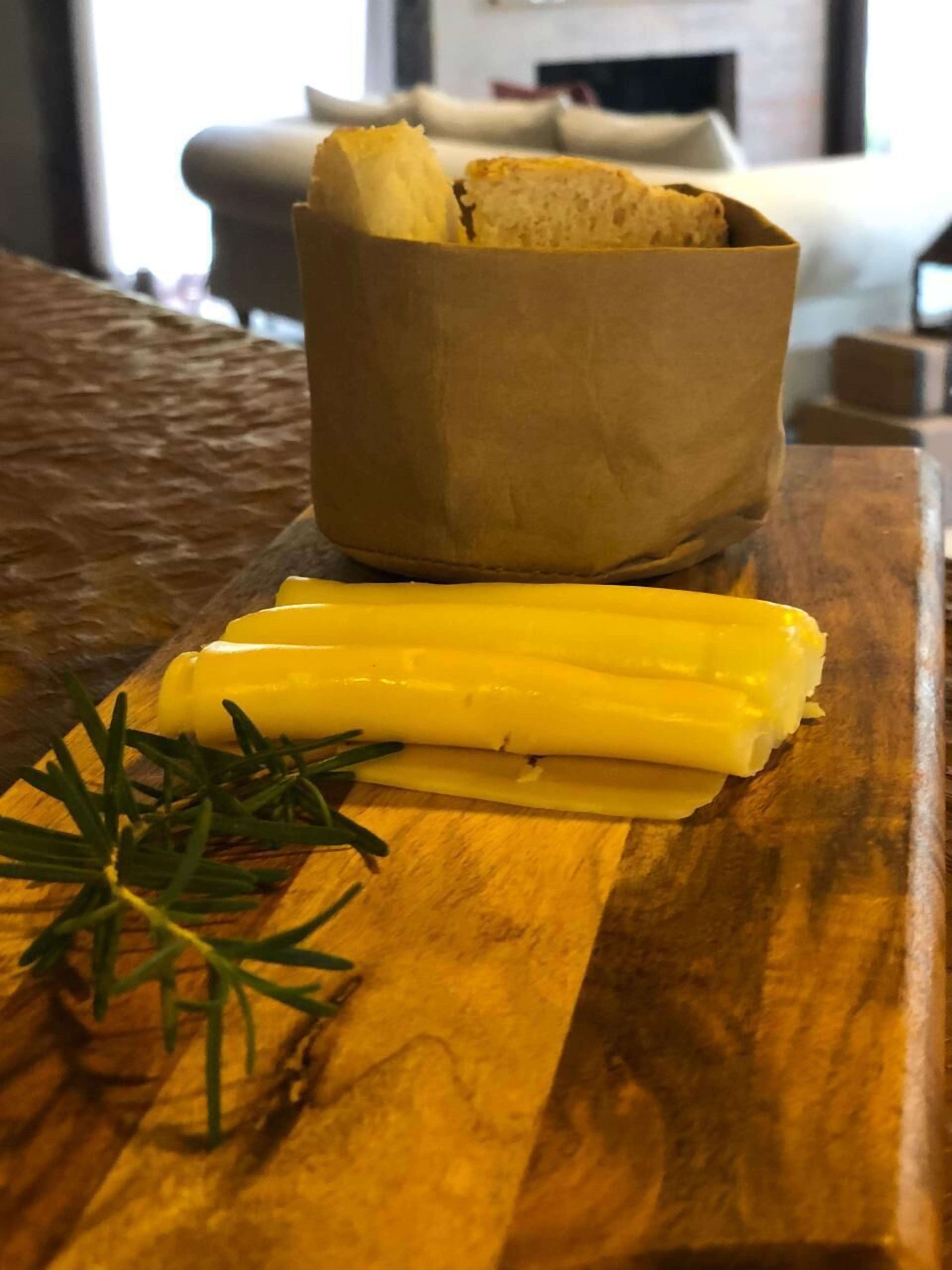 Una tabla de madera con queso, una ramita de romero y un vaso de papel con pan.