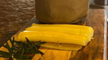 Una tabla de madera con queso, una ramita de romero y un vaso de papel con pan.