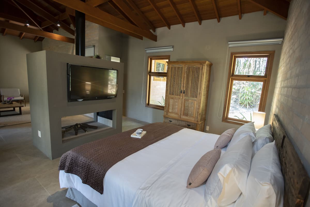 Un dormitorio con una cama grande, un televisor de pantalla plana en la pared, un armario de madera y una ventana que deja entrar luz natural.