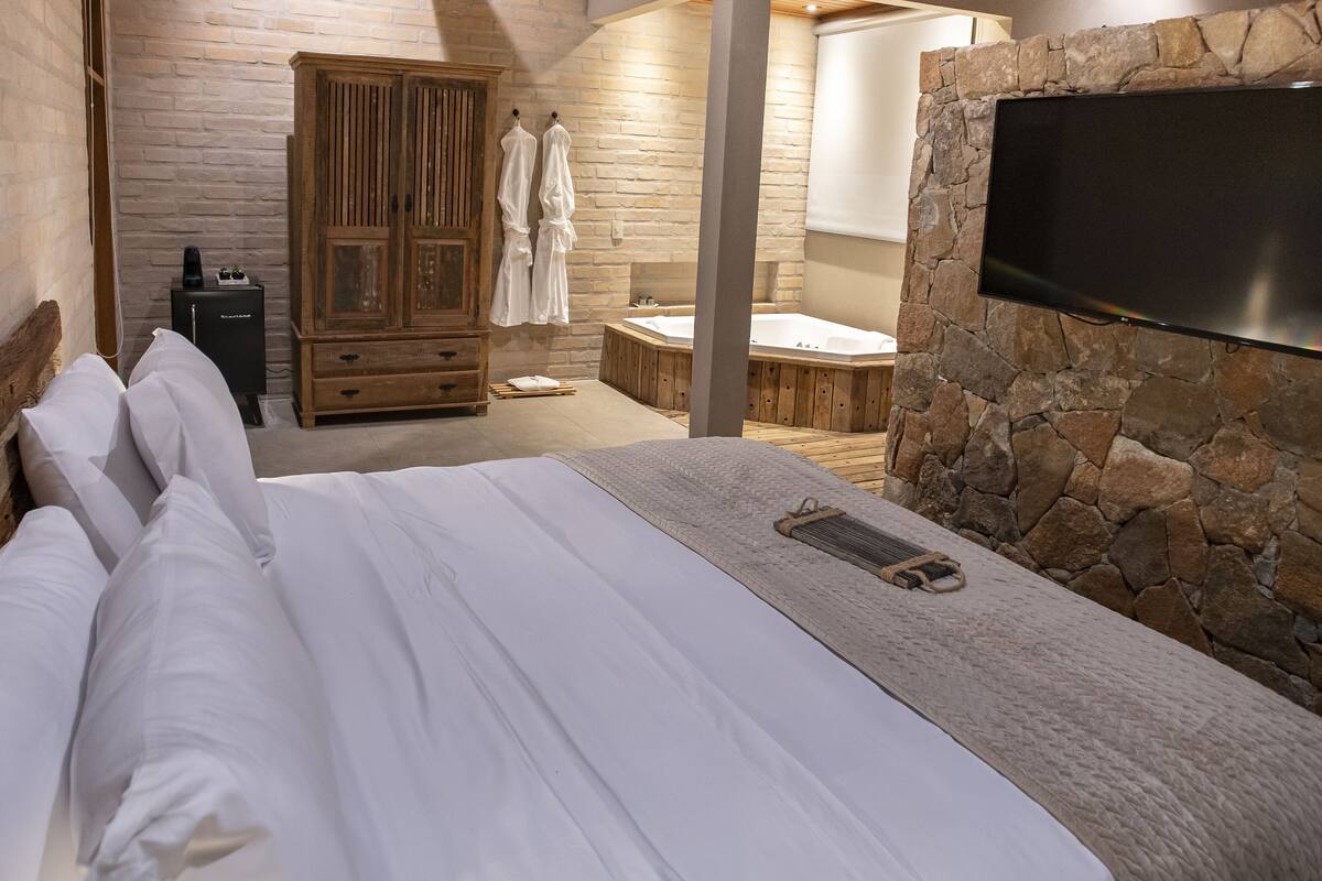 Un dormitorio con una cama grande, un armario de madera, una pared de piedra y un televisor de pantalla plana montado en la pared.